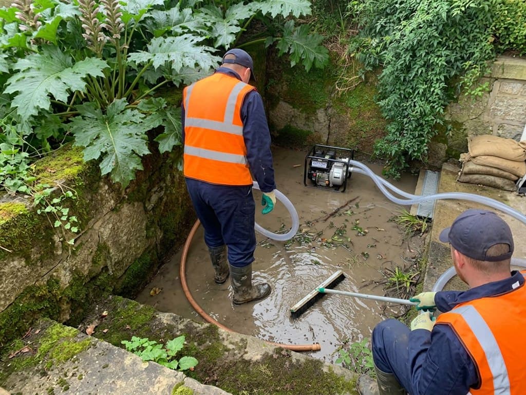Operarios de Net & Clair Barbanza S.L.U. achicando y baldeando el agua encharcada en el patio de una vivienda